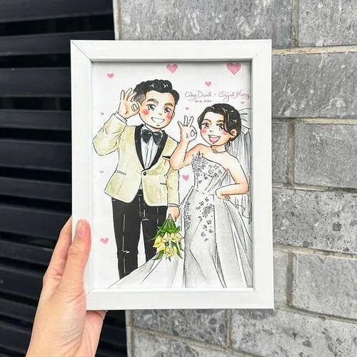 Ảnh bàn tay cầm khung tranh chibi cô dâu chú rể, phong cách tối giản hiện đại