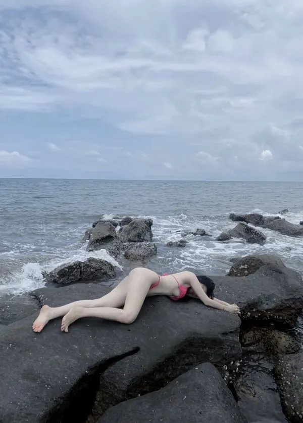 Nàng nằm trên cát trắng, bikini gọn, tóc xõa che mặt, vai trần mịn, dáng thư thả mà gợi.