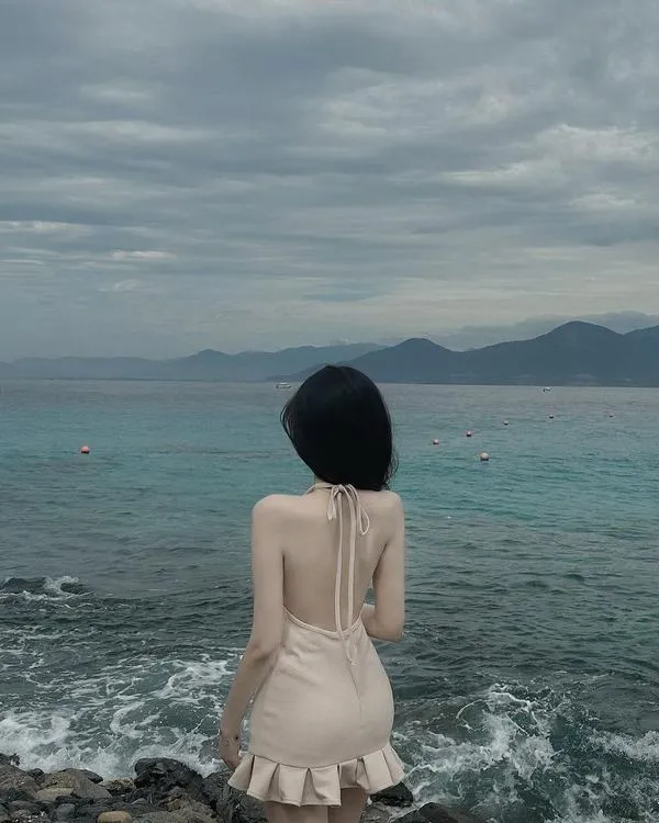 Bóng râm dịu trên bờ biển, nàng che mặt, bikini cạp cao, eo thon rõ, đôi chân dài nổi bật.