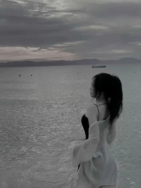 Cô gái trong khung trời xám, đứng sát bờ biển, tóc dài rối nhẹ, bikini ôm dáng, vẻ buồn mà cuốn.