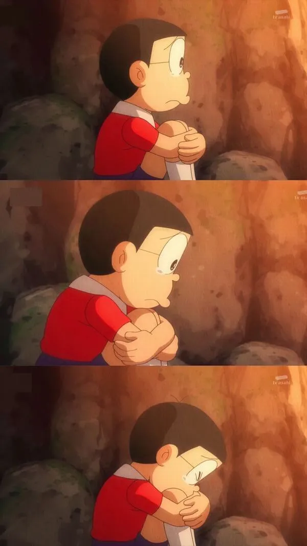 Nobita ngồi một góc, ôm chặt lấy mình, mắt ướt, tủi thân dồn lại thành im lặng.