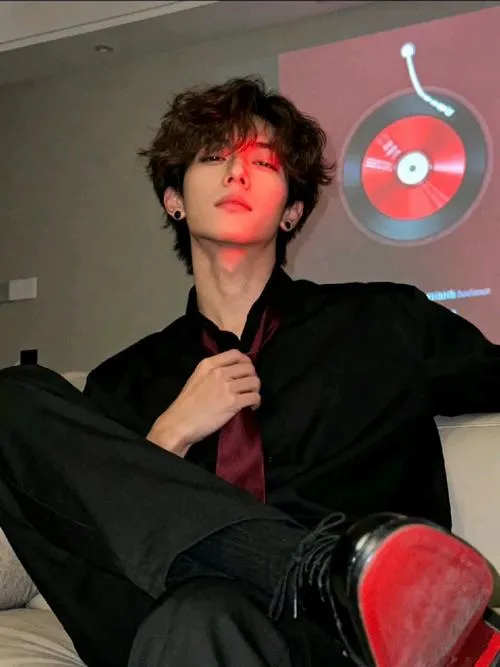 Trai phong trần diện đồ đen, ánh đèn đỏ làm nền, dáng ngồi thả lỏng vẫn ngầu.