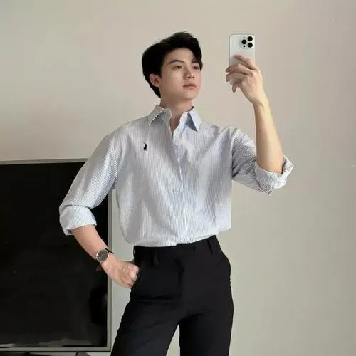 Ảnh nam thần Việt đứng trước gương áo trắng, kiểu tóc gọn gàng, ánh mắt tập trung.