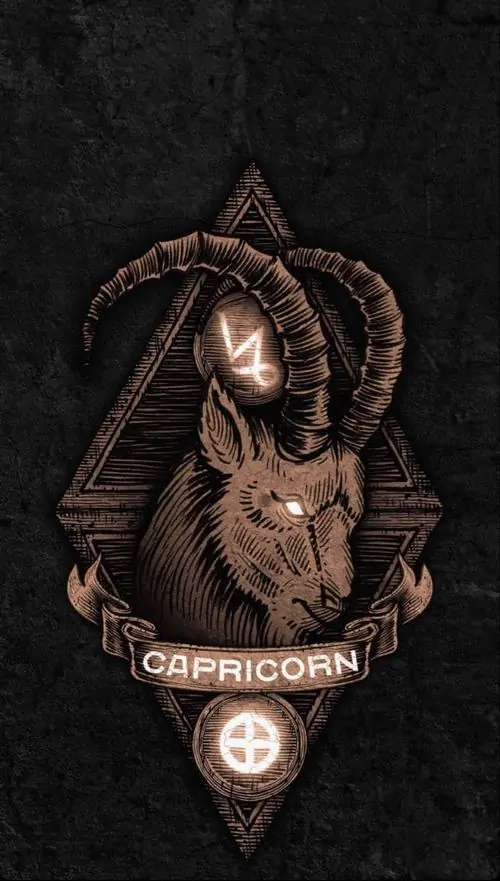 Bàn tay tối màu nâng mô hình đầu dê nhỏ trên nền đen, ánh đồng hắt vào sừng và mặt tạo cảm giác gần, ảnh hợp ai thích biểu tượng Ma Kết kiểu trầm lạ