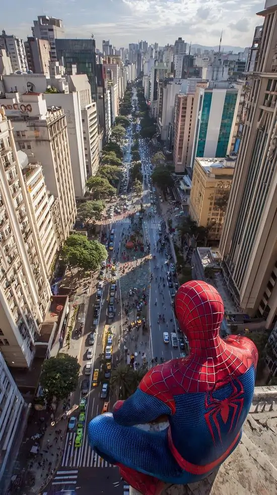 Người nhện trong bộ đồ xanh đỏ ngồi chênh vênh trên mép nhà cao tầng, nhìn xuống đại lộ đông xe theo góc từ sau lưng tạo cảm giác rơi sâu rất hợp màn hình Samsung