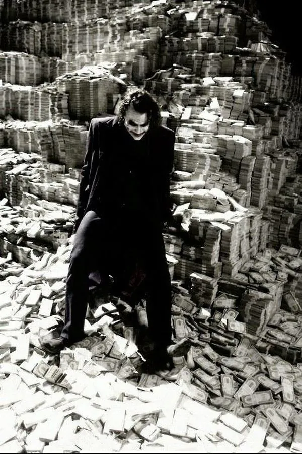 Từ góc xa, một bóng người mặc đồ tối đứng giữa bậc thang và đống gạch vụn, sắc đen trắng dày hạt khiến ảnh nền gã hề mang cảm giác lạnh và cứng như phim cũ