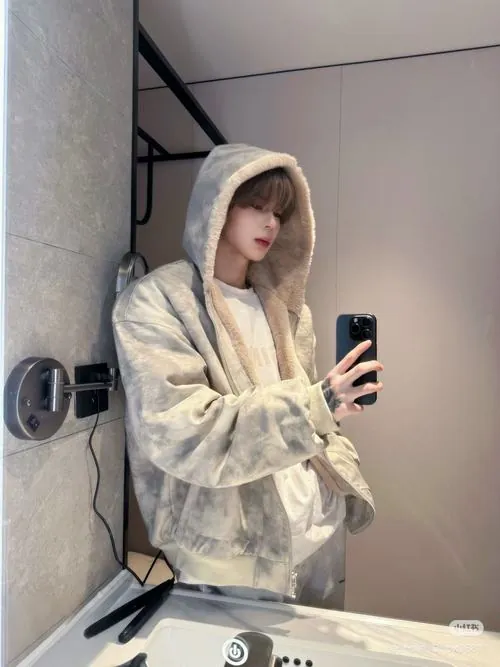 Ảnh mỹ nam mạng Trung chụp gương trong áo khoác trắng có mũ, điện thoại che mặt giữa không gian kim loại sáng lạnh.