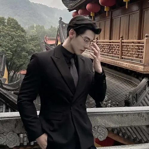 Ảnh chủ tịch lịch lãm mặc vest đen trên ban công gỗ, dáng cúi đầu suy nghĩ giữa khung cảnh núi xanh phía sau.