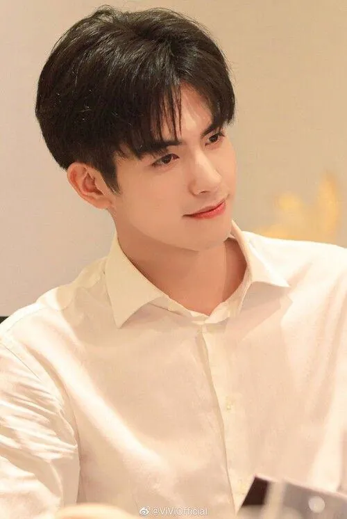 Chàng trai xem bản thiết kế trên bàn kính, sơ mi trắng dài tay và măng séc mở nhẹ khi bàn tay chống xuống.