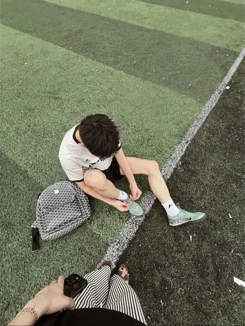 Ảnh trai đá bóng che mặt có nhân vật áo trắng ngồi sát vạch biên, ôm đầu vào cánh tay cạnh đôi giày đặt trên cỏ.