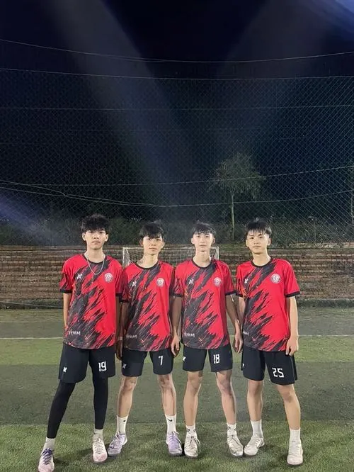 Ba cầu thủ áo đỏ đen đứng gần khung thành dưới ánh đèn đêm, vẻ mặt bình tĩnh sau một tình huống thi đấu.