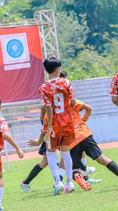 Nam cầu thủ mặc áo cam số 9 quay lưng chạy trên sân, áo đấu nổi bật giữa nền phông đỏ và ánh sáng ngoài trời.