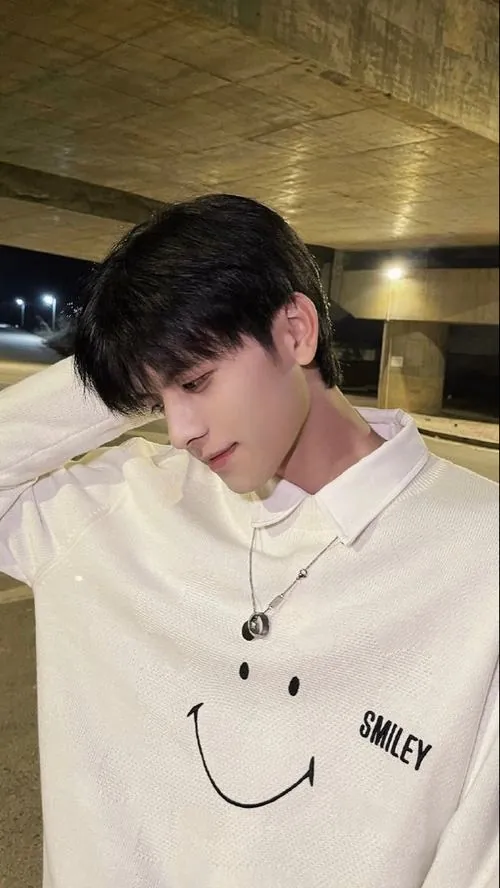 Ảnh hot boy xứ Trung ngồi nghiêng trên ghế, sơ mi trắng cài gọn, ánh đèn vàng làm gương mặt cúi xuống thêm thanh tú.