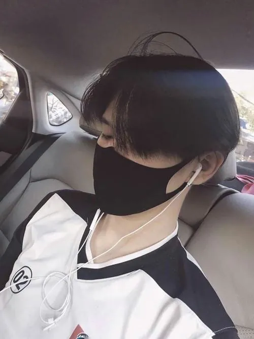 Dưới mái ga tàu phủ sương, người mẫu nam mặc áo dạ xanh đậm, cầm vé giấy, khẩu trang xám hợp với buổi sớm lạnh.
