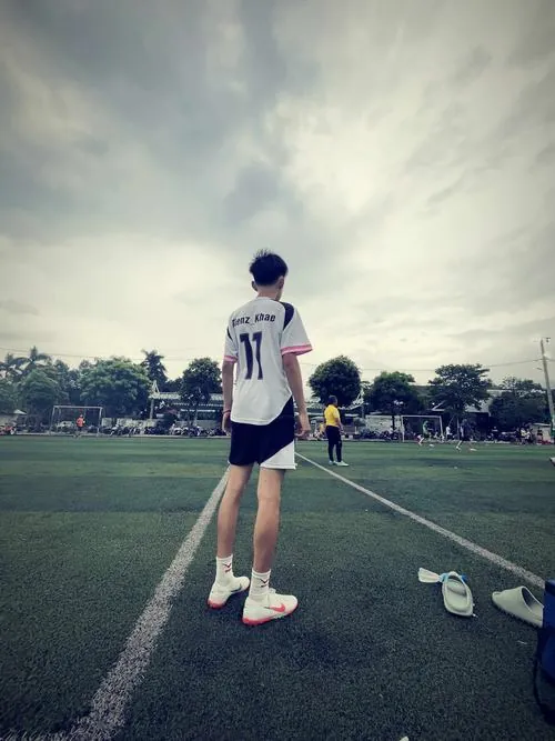 Trong ga tàu yên ắng, nam sinh ôm túi bóng và cúi sau tấm vé, tất cổ cao lộ rõ dưới quần thể thao.