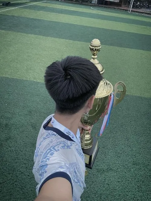 Ở lối hầm sân vận động, chàng trai kéo cổ áo che nửa mặt, bước qua dãy tường bê tông với túi đựng giày trên vai.