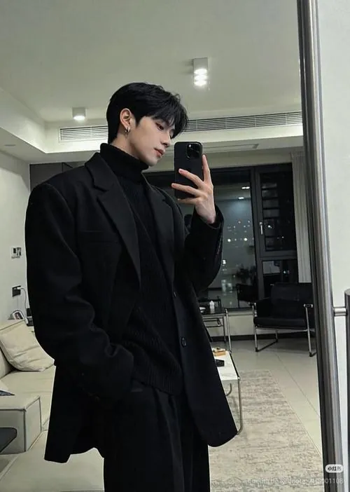Bộ vest đen được ghi lại qua gương trong phòng sáng, điện thoại che mặt và cách đứng thẳng nhấn vào phong cách tối giản.