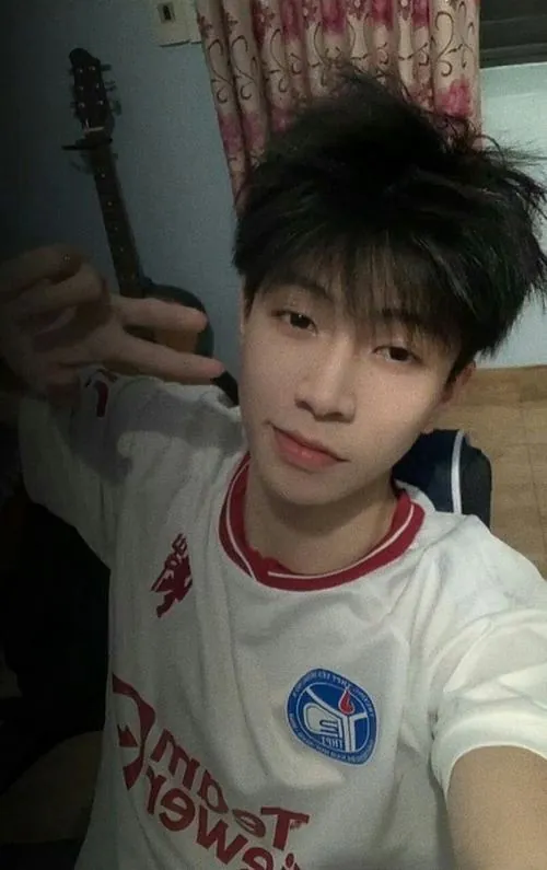 Cậu bạn áo trắng viền đỏ chụp selfie trong phòng ngủ, gương mặt sáng và ánh nhìn bình tĩnh tạo cảm giác rất thân quen.