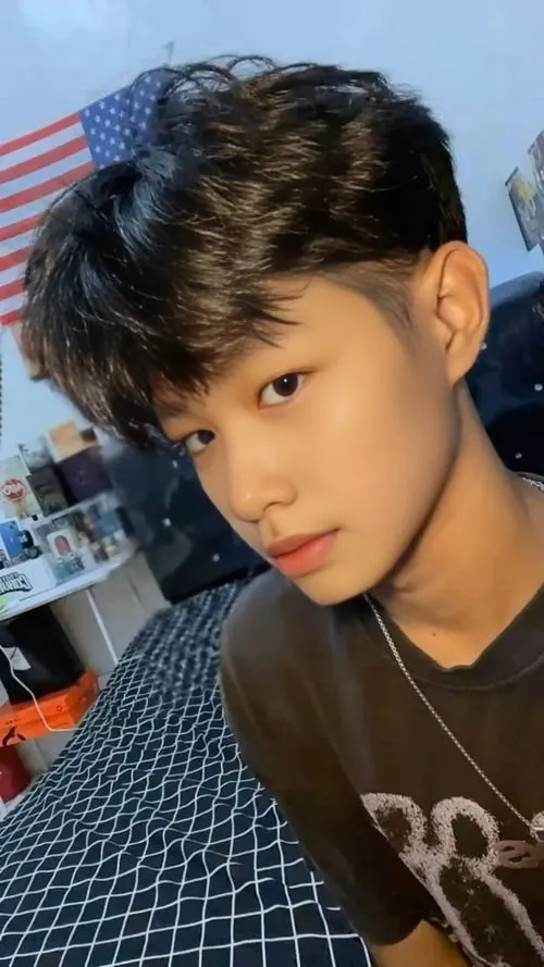Nam sinh tóc đen selfie trong phòng, áo tối màu và sợi dây chuyền nhỏ tạo cảm giác gọn gàng, gần gũi như cậu bạn cùng lớp.