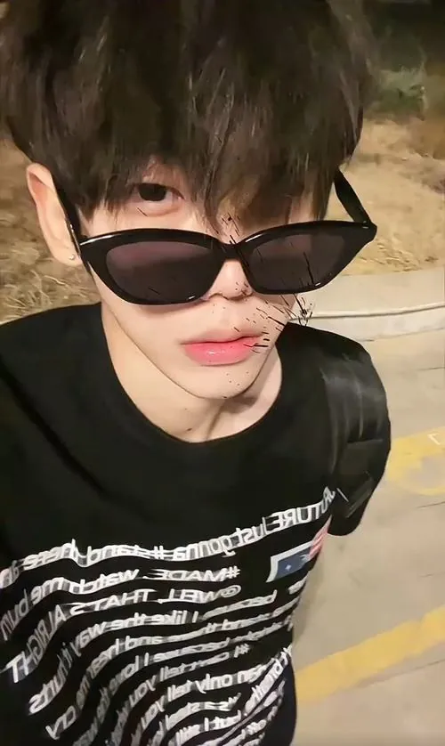 Cậu bạn mặc áo đen đeo kính râm, tạo dáng selfie gần ống kính với bàn tay chạm môi, phong cách trẻ trung và hơi nghịch.