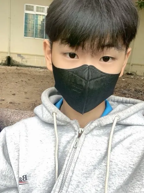 Bạn nam đeo khẩu trang đen và hoodie xám ngoài trời, đôi mắt nhìn thẳng tạo cảm giác hiền lành, mộc mạc.