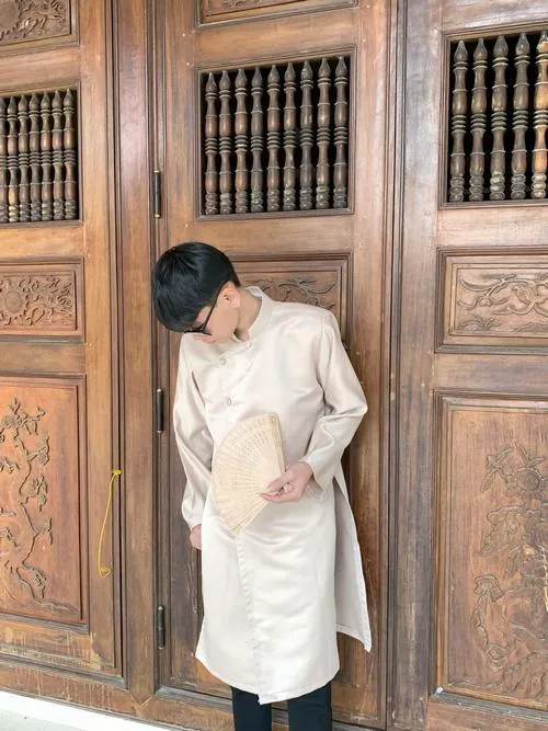 Nam sinh mặc đồ trắng tựa bên tủ gỗ, một tay đặt lên tóc, khung ảnh mang màu học đường giản dị.