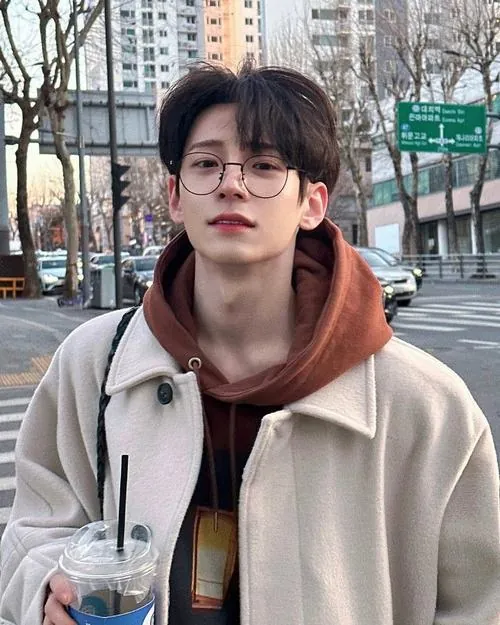 Ảnh trai k12 phối áo khoác sáng màu với hoodie nâu, đứng trên phố và nhìn xa, nét mặt bình thản nhưng vẫn rất trẻ trung.