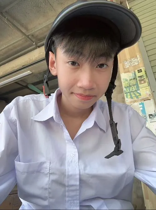Nam sinh mặc áo sơ mi trắng ngồi trong không gian hẹp, dây tai nghe và nụ cười nhẹ tạo vẻ học trò gần gũi.