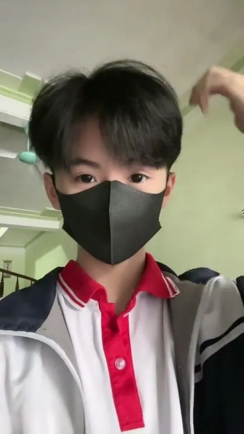 Giữa thư viện yên tĩnh, nam sinh cấp hai dùng cuốn sách giáo khoa mở rộng che mặt, phía sau là những kệ sách cao.