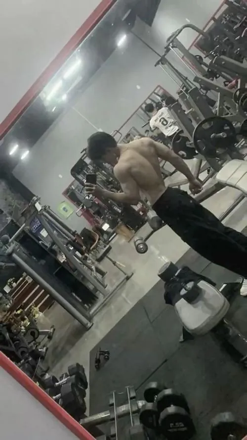 Ảnh trai tập gym đẹp có góc máy nghiêng trong gương, nam gymer cúi người tập trung, xung quanh là máy móc và ánh đèn mạnh.