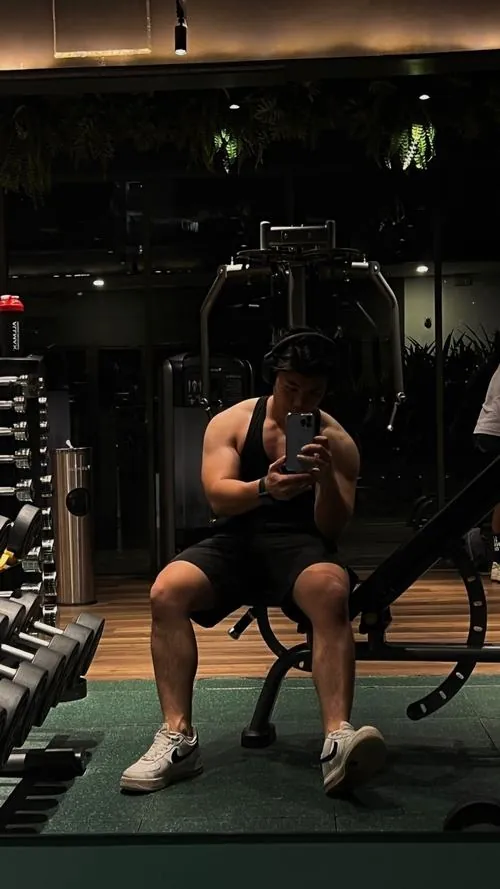 Tại khu kiểm tra thể trạng, một nam gymer đứng cạnh bảng chỉ số tỷ lệ mỡ, tay cầm bình nước thể thao sau buổi tập nhẹ.