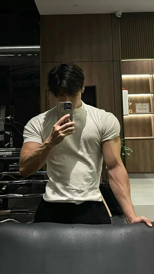 Huấn luyện viên cá nhân quan sát học viên nam chỉnh tư thế nâng tạ từ sàn trên bệ tập gánh tạ đa năng.