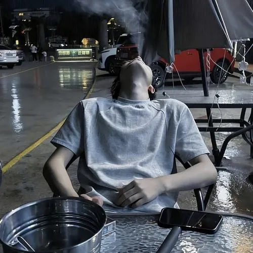 Nam thanh tú che mặt bằng măng tô đen dáng dài, đứng tựa góc tường xám tối giản với bàn tay thắt lại che gần hết nụ cười.