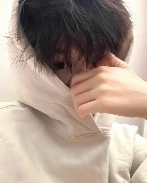 Nam người mẫu khoác áo vest nhung đỏ đứng trong studio, dùng các ngón tay thon dài vuốt nhẹ từ trán xuống sống mũi che đi ánh nhìn sắc lạnh.