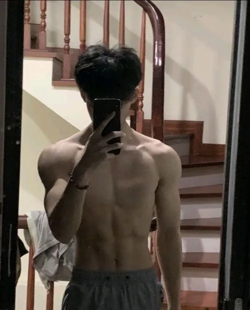 Chàng trai đứng trong rừng cao su mùa trút lá, giơ một chiếc lá khô to bản che ngang mắt dưới dải nắng xuyên qua kẽ lá.