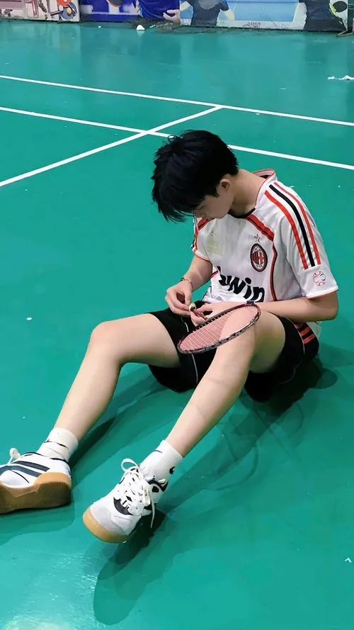 Chàng trai ngồi bệt thư giãn trên sàn thi đấu, hai tay tỉ mỉ căn chỉnh lại độ dẻo của dây quấn cán vợt.